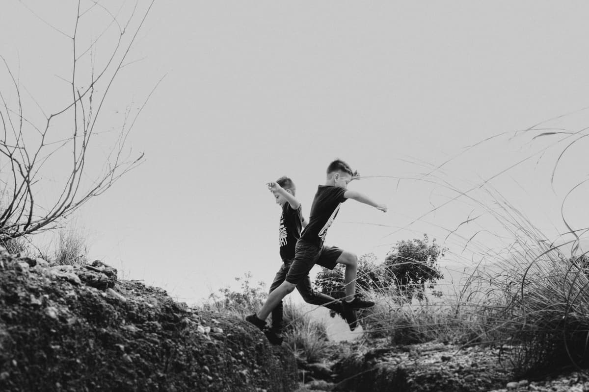 Twin boys leaping across rocks